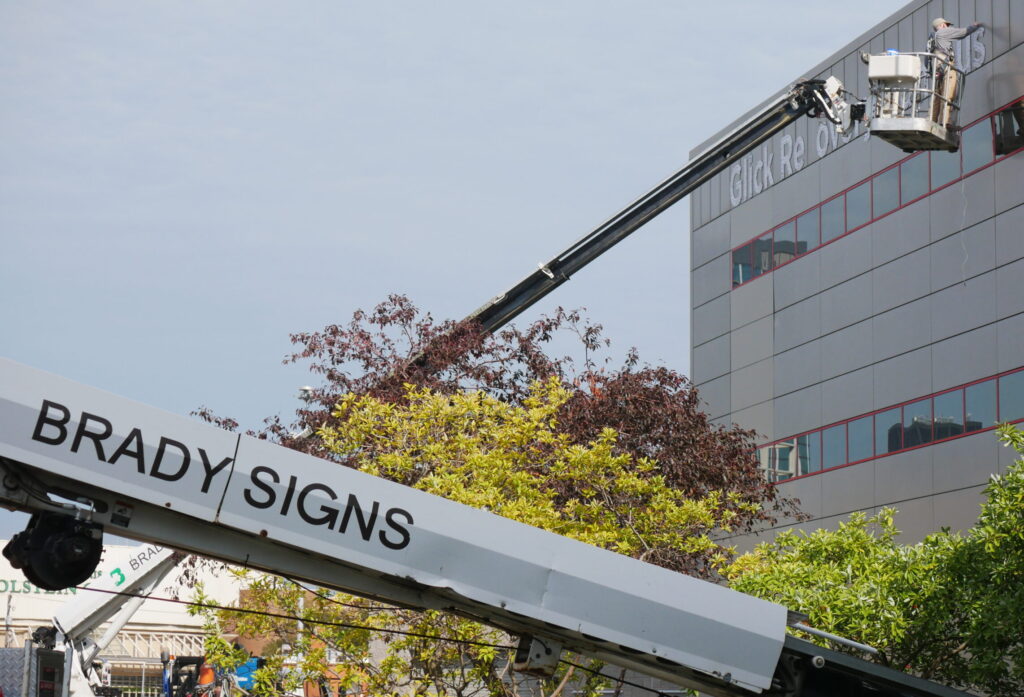 Brady Signs technician in an aerial lift installing channel letters on a multi-story commercial building